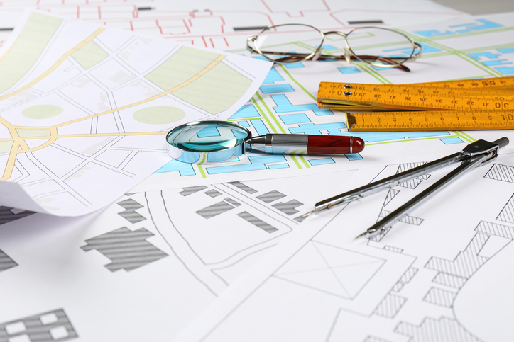 Office stationery, magnifying glass and folding ruler on cadastral maps of territory with buildings